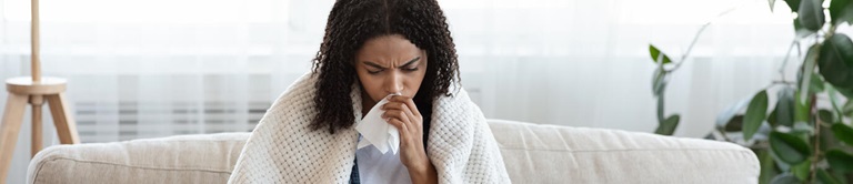 Sick woman sitting on a couch holding a tissue to her nose