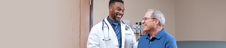 Young middle aged male doctor talking with an older male patient in an exam room.